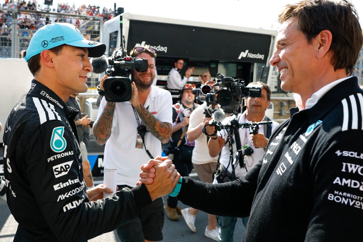 Russell shaking hands with Mercedes boss Wolff at F1 track, both smiling
